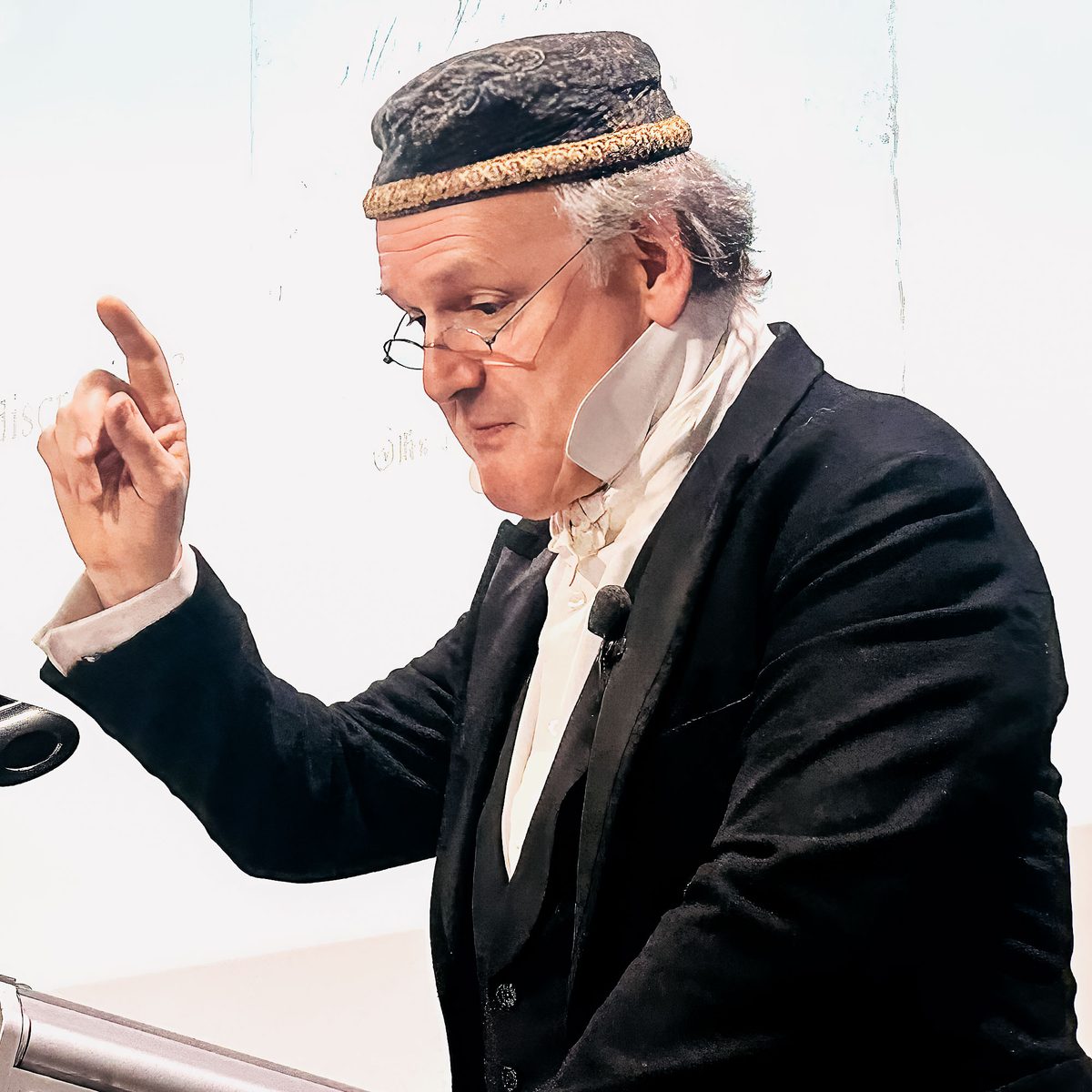 Michael Quast als Johann Anton André, mit erhobener Hand gestikulierend vor der projizierten Titelseite.